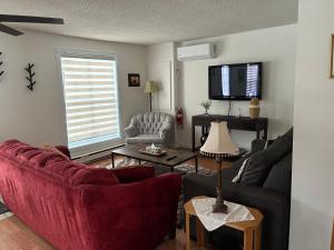 a living room with a red couch and a tv at Floral'Anse in LʼAnse-Saint-Jean