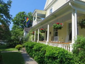 a yellow house with a porch with a flag on it at Cooperstown Bed and Breakfast in Cooperstown