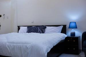a bed with white sheets and a blue lamp on a night stand at Winners Home in Kumasi