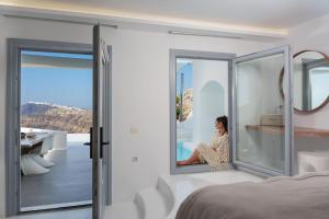 a woman sitting on a window sill in a bedroom at Nelya Suites in Megalochori