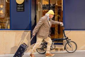an older man walking a bike and pulling a suitcase at Hôtel des Arts Montmartre in Paris