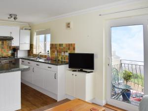 a kitchen with white cabinets and a tv and a balcony at Dicks View in Ventnor