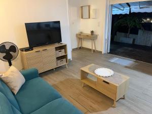 a living room with a blue couch and a flat screen tv at Logement cosy avec piscine proche de l'aéroport in Ducos