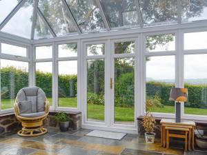 a conservatory with a chair in a room with windows at Green Lane Cottage in Newtown