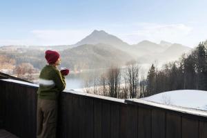 a woman standing on a balcony looking out over a lake at Arabella Jagdhof Resort am Fuschlsee, a Tribute Portfolio Hotel in Hof bei Salzburg