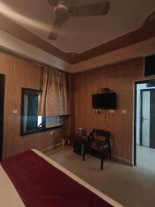 a bedroom with a bed and a chair and a television at Hotel Aashray in Haridwār