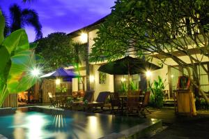 a pool with chairs and tables and umbrellas at night at Sari Villa Sanur Beach in Sanur