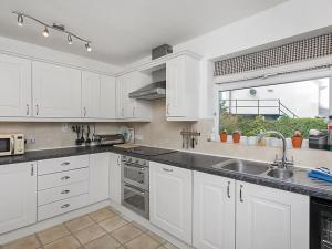 a kitchen with white cabinets and a sink and a window at Gosteg in Moelfre