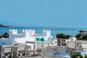 a restaurant with white tables and chairs and the ocean at Kanale's Rooms & Suites in Naousa