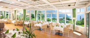 a room with white tables and chairs and windows at Hotel Hollweger in Sankt Gilgen