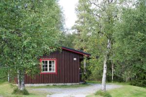 a red cabin with a window in the woods at Sörmons Stugby in Ljusnedal