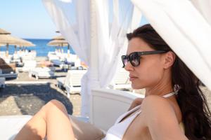 a woman in sunglasses sitting on a chair at the beach at La Mer Deluxe Hotel & Spa in Kamari