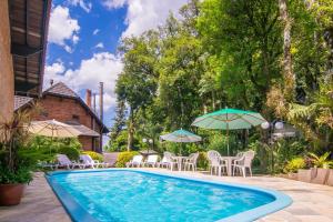 a swimming pool with patio furniture and umbrellas at Hotel Azaleia in Gramado