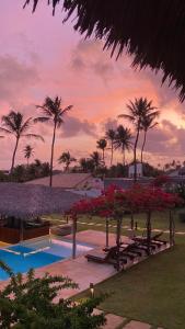 a resort with a pool with red flowers and palm trees at Pousada Casa Caju Bangalows in Cumbuco