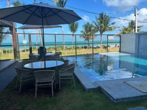 a table and chairs with an umbrella next to a swimming pool at Prive Beira Mar Tamandare in Tamandaré