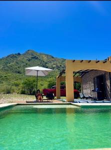 a man sitting under an umbrella next to a swimming pool at GinTonic Rancho in San Luis