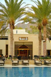 a pool with palm trees in front of a restaurant at Sheraton Oman Hotel, Muscat in Muscat