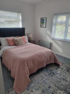 a bedroom with a bed with a pink blanket and two windows at Halwyn View in St Austell
