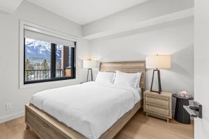 a white bedroom with a large bed and a window at Modern mountain luxury with stunning views in Canmore