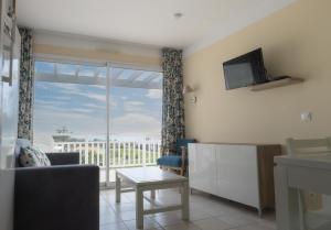 a living room with a couch and a tv and a window at Les Sables-d'Olonne - Vue Mer, Terrasse, Wifi Fibre & Piscine, à 2 pas de l'Océan - E101 in Les Sables-d'Olonne