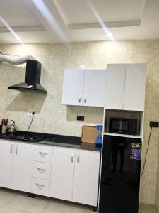 a kitchen with white cabinets and a black refrigerator at Dinems Apartment in Ikeja