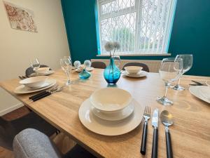 a wooden table with plates and glasses on it at Very Spacious 4 Bedroom house with large garden in Leamington Spa