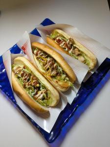 three hot dogs with toppings on a blue tray at BigTree JUDOハウス in Urazoe