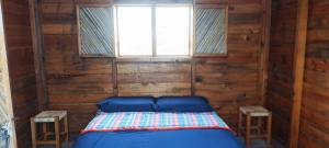 a bed in a wooden room with two stools at Chacahua Cabañas LAUD in Guayabas