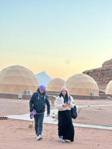two people walking in front of domes in the desert at Jihad camp in Disah