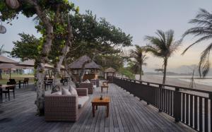 a wooden deck with couches and tables on the beach at MERUSAKA Nusa Dua in Nusa Dua