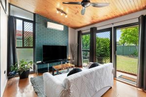 a living room with a white couch and a flat screen tv at Pukeko Guesthouse - Relax in Redcliffe in Redcliffe