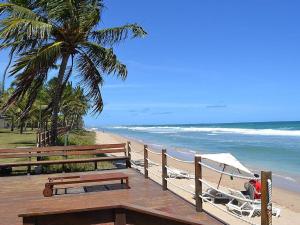 eine Holzterrasse mit Stühlen und einem Sonnenschirm am Strand in der Unterkunft Flat no Beach Class Resort in Porto De Galinhas