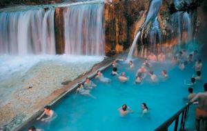 a group of people swimming in a pool in front of a waterfall at Hotel Edem in Kato Loutraki