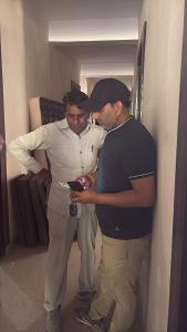 two men standing in a room looking at a cell phone at Vansh Residency Couple Friendly Near Rajiv Chowk Gurgaon in Gurgaon