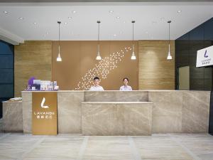 two people standing behind a counter in a lobby at Lavande International Hotel Guangzhou Baiyun International Airport Renhe Metro Station Branch - Free Shuttle Bus to Guangzhou Baiyun International Airport in Guangzhou