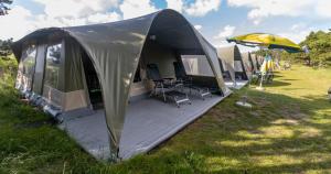 a tent with chairs and an umbrella in a field at Glamlodge Ameland direct aan het strand in Nes