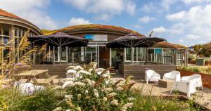 a building with chairs and umbrellas in front of it at Duynlodge Ameland direct aan het strand in Nes