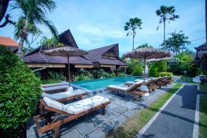 a pool with chairs and umbrellas next to a house at The Calmtree Bungalows in Canggu