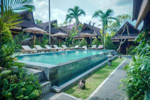 a swimming pool in a resort with chairs and trees at The Calmtree Bungalows in Canggu
