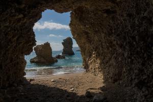 a view of the ocean through a rock cave at Archipelagos Apartments in Arkasa