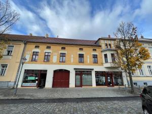 a large yellow building with red doors on a street at Pension am Markt Luckenwalde in Luckenwalde