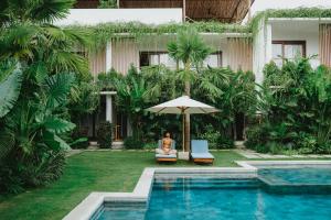a woman sitting in a chair under an umbrella next to a pool at Porter Boutique Hotel & Lifestyle in Kuta Lombok