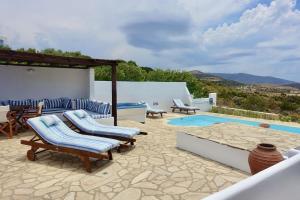 a patio with lounge chairs and a swimming pool at Villa E - Kamari Village in Kastraki
