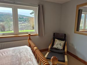 a bedroom with a bed and a chair and two windows at The Studio in Drumnadrochit