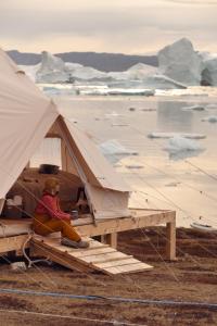 a person sitting inside of a tent with an iceberg at Nomad Greenland Camp Saqqaq in Saqqaq