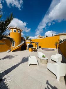 a patio with white chairs and a yellow building at Casa Indigo Mazarron in Mazarrón