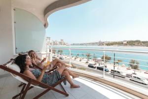 two women sitting in chairs on a balcony with a view of the ocean at The Strand Waterfront Apartment with 3 Bedrooms, 4 Bathrooms, Private Garage in Sliema