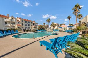 a swimming pool with blue chairs and palm trees at Toes In The Water II in Padre Island