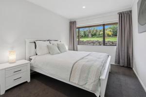 a white bedroom with a white bed and a window at Clay Cottage in Waimauku