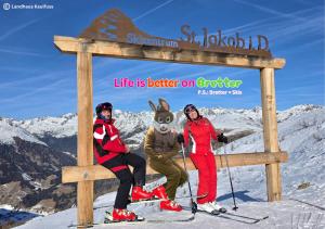 three people sitting next to a sign on a ski slope at Landhaus Kaulfuss in Sankt Jakob in Defereggen